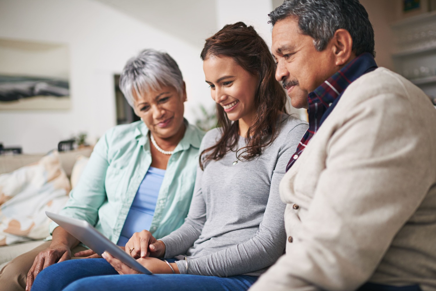 Familia hispana sonriendo mientras revisa información en una tablet en casa, representando unión, protección y planificación familiar.